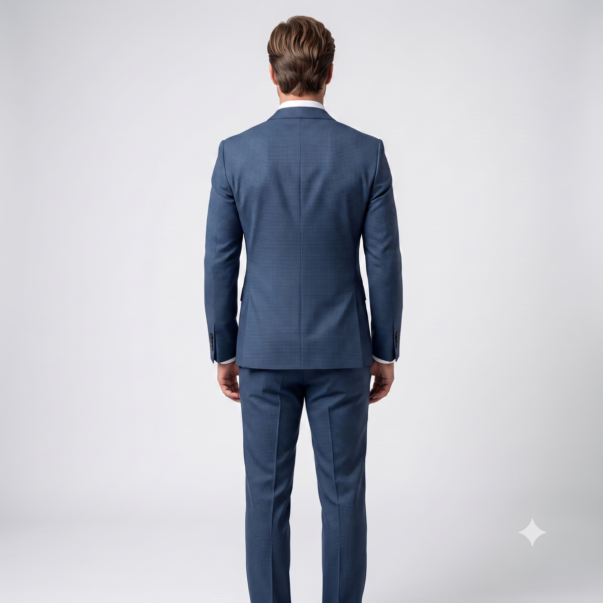 A man viewed from the back wearing a navy blue suit with a white collared shirt, standing against a light gray studio background.
