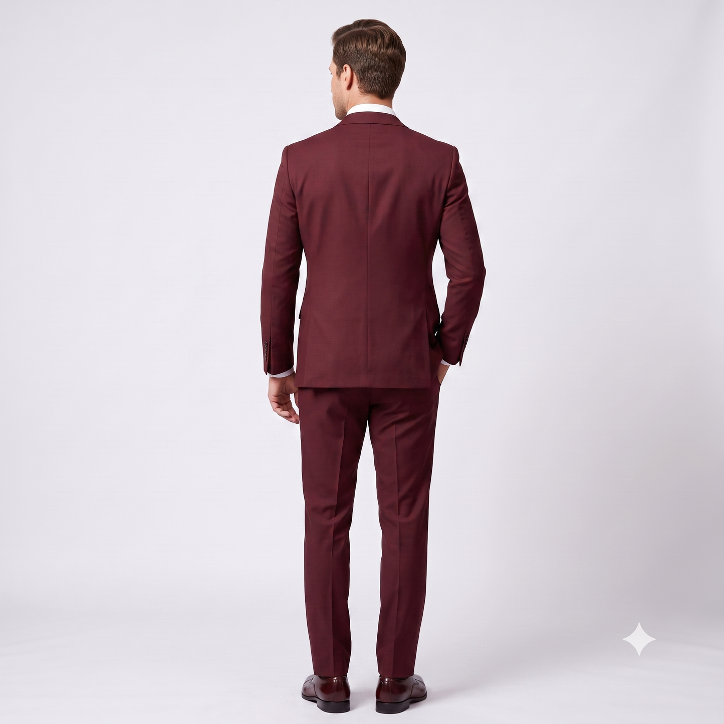 A man viewed from behind wearing a matching burgundy suit, white dress shirt, and dark brown dress shoes against a light gray studio background.