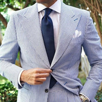 Man wearing a blue and white striped suit with a navy tie outdoors.