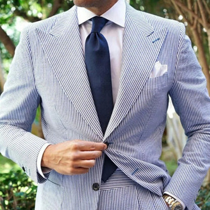 Man wearing a blue and white striped suit with a navy tie outdoors.