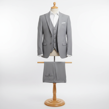 Three-piece light grey men’s suit displayed upright on a wooden stand. Slim-fit jacket and matching waistcoat with clean tailoring, paired with coordinated trousers folded neatly over the display bar. Styled with a white dress shirt. Clean studio background with soft, even lighting. 250:250