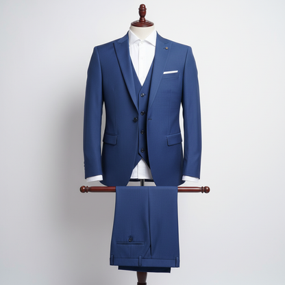 Three piece royal blue men’s suit displayed upright on a wooden stand. Slim-fit jacket and matching waistcoat with clean tailoring, paired with coordinated trousers folded neatly over the display bar. Styled with a white dress shirt. Clean studio background with soft, even lighting. 250:250