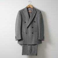 Two-piece grey men’s suit displayed on wooden hangers, featuring a double-breasted jacket in textured woven fabric with subtle patterning and matching trousers. Presented in a clean studio setting with soft lighting emphasizing the fabric texture and tailored fit.